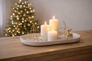 Plateau en céramique posé sur un buffet en bois brut, contenant trois bougies blanches et des décorations en métal doré minimalistes