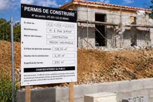 Panneau réglementaire de permis de construire installé sur un terrain où une maison est en construction